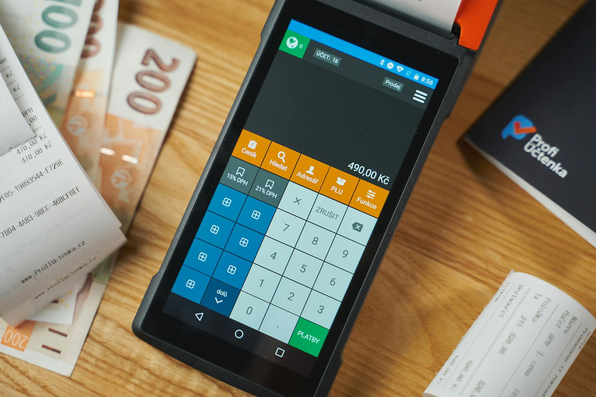 Close-up of a digital payment terminal on a wooden desk with receipts and currency notes.